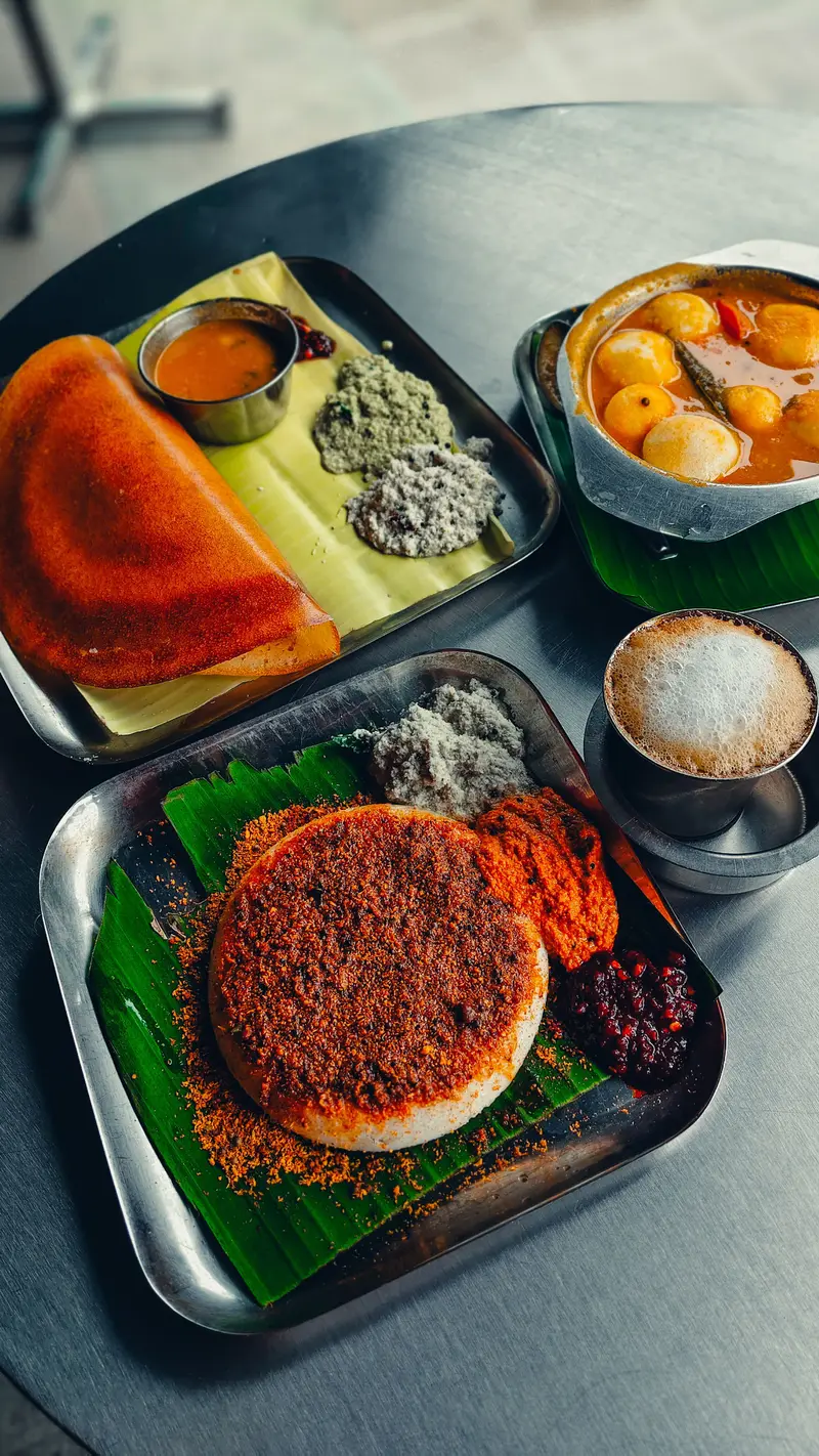 Steel trays on banana leaf with a dosa, a podi-dusted uttapam, chutneys and a frothy filter coffee