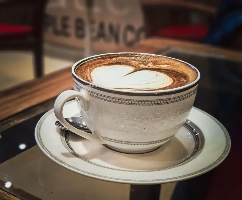 A cappuccino with a heart in the foam, in a white cup and saucer on a glass table