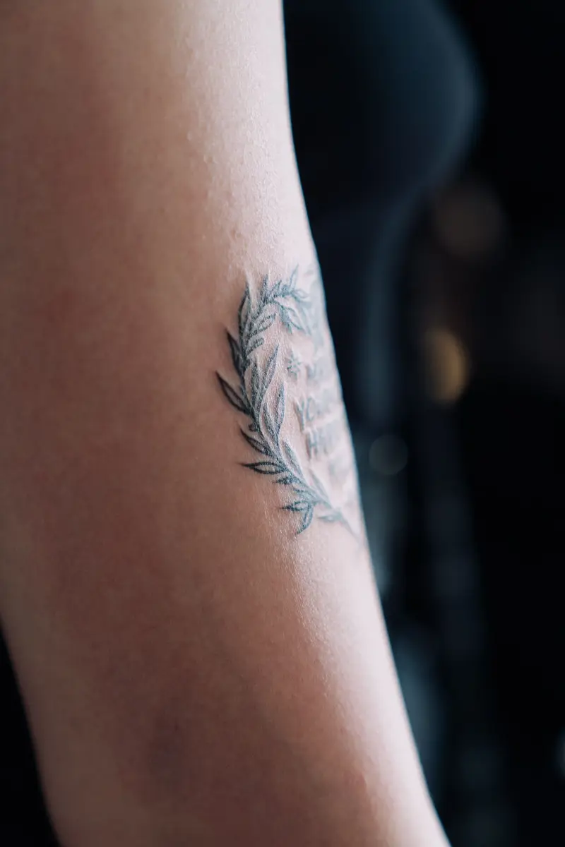 Small fine-line leaf tattoo on the back of an upper arm